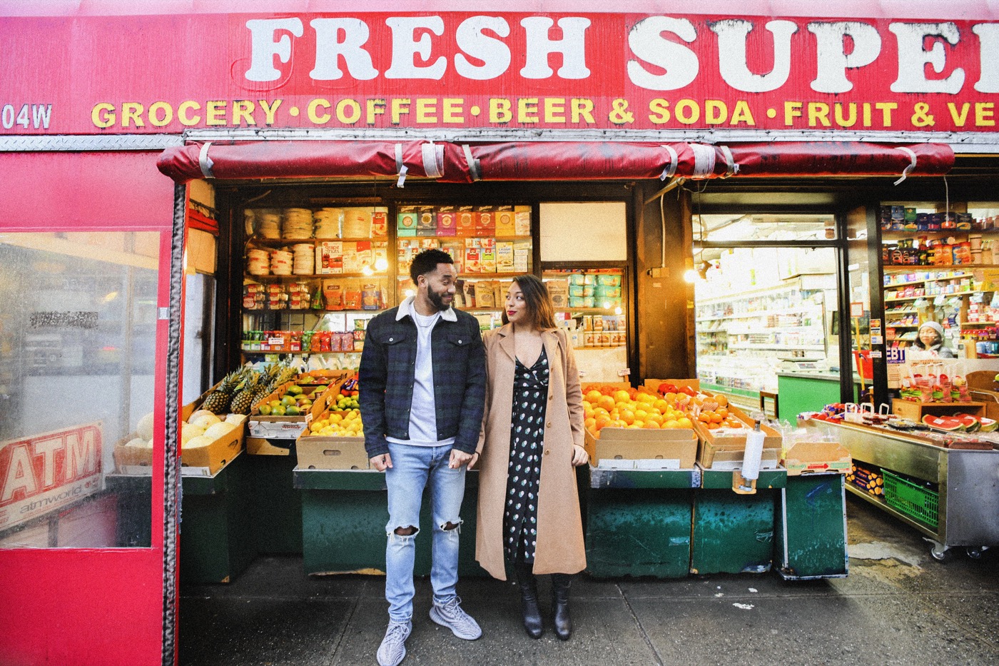 Couple in front of a red grocery storefront amid fruit stands