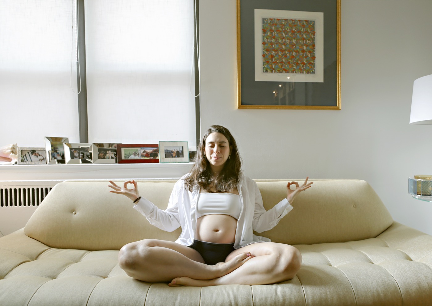 Pregnant woman meditating cross-legged on a cream couch