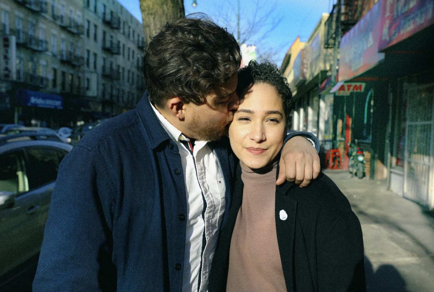 Man kissing a woman's temple on a sunlit street