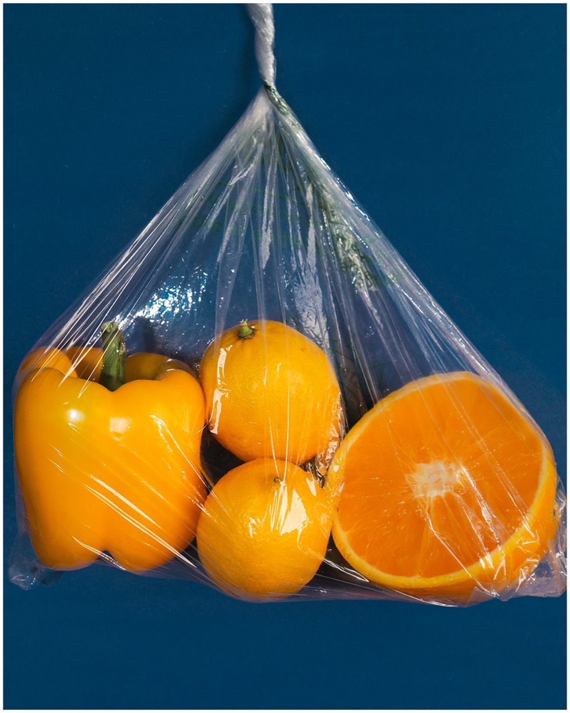 Oranges in a mesh produce bag against deep blue